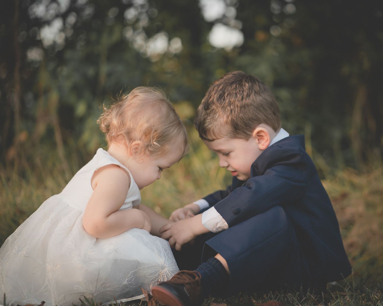 Children in formal wear share quiet moment together outdoors.