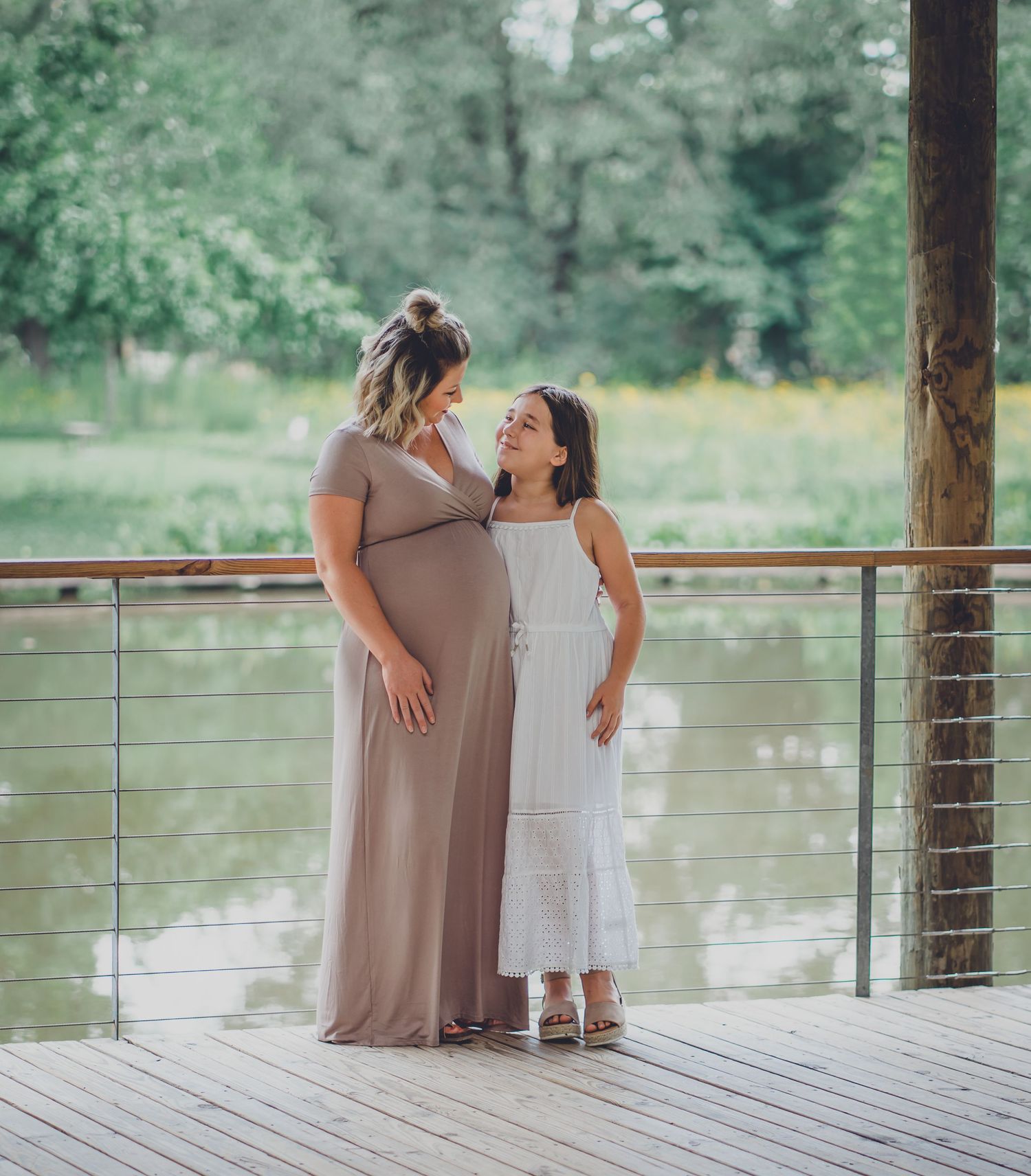Mother and child share a tender moment on wooden deck overlooking water.