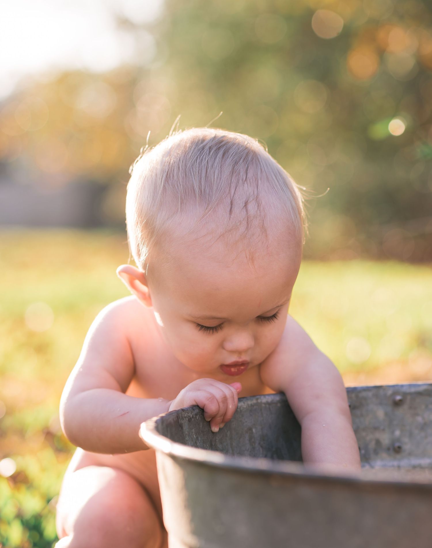 Baby exploring metal washtub during sunset in garden setting.