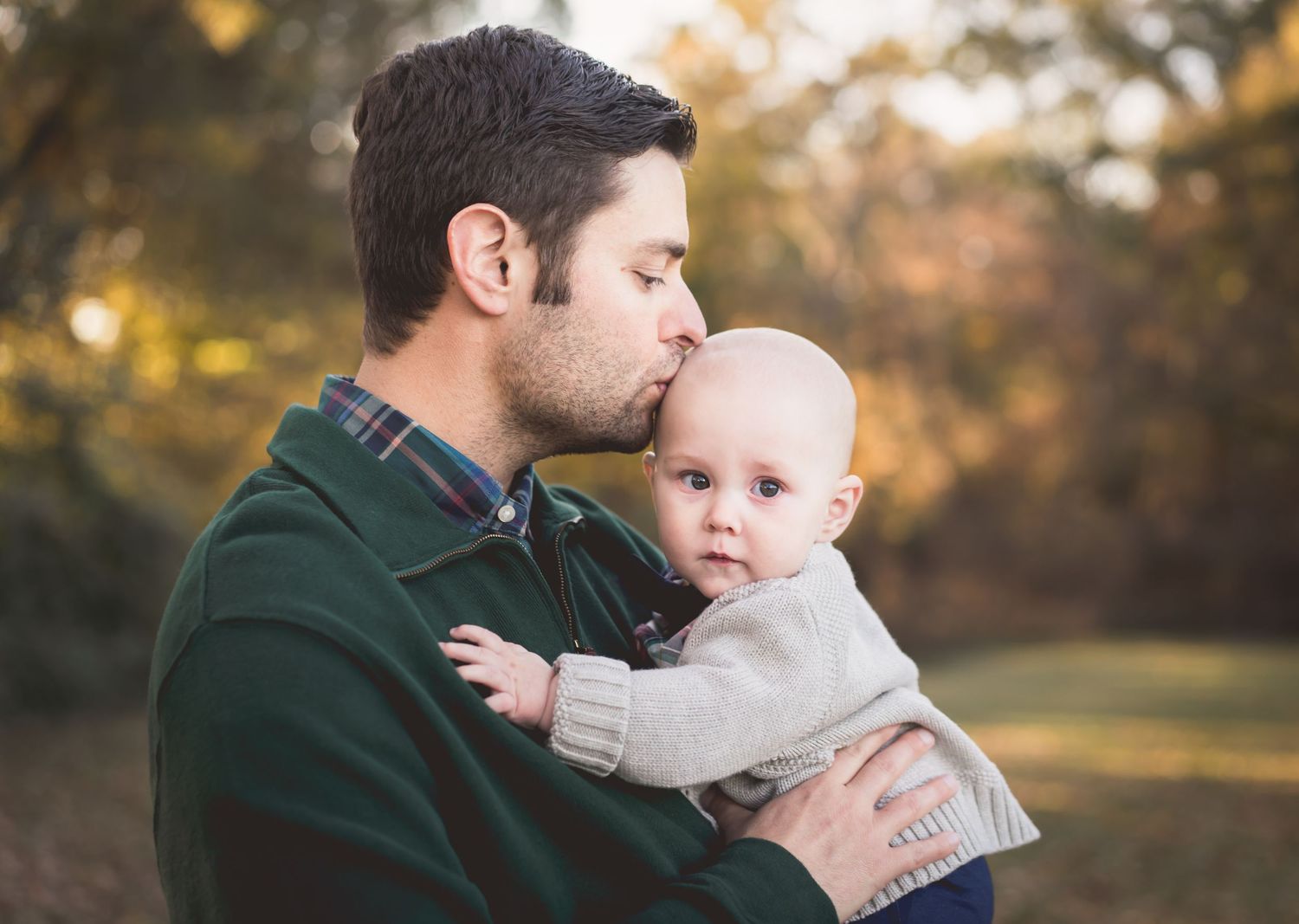 Portrait of tender moment between parent and baby outdoors in green sweater.