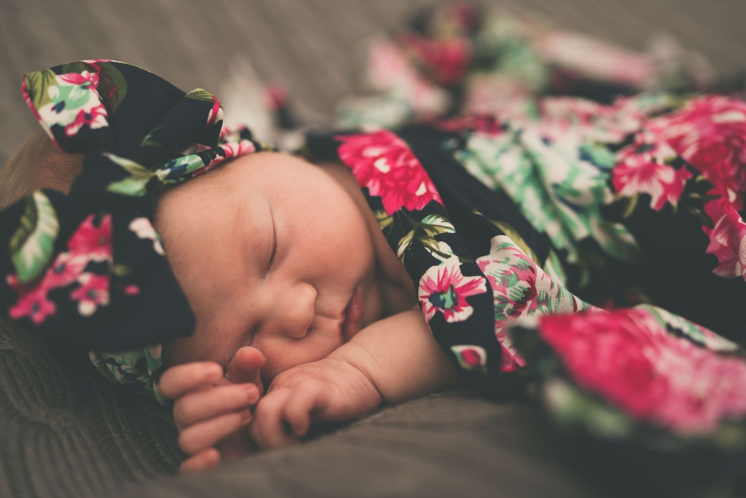 Newborn baby sleeping peacefully in floral outfit on gray textured surface.