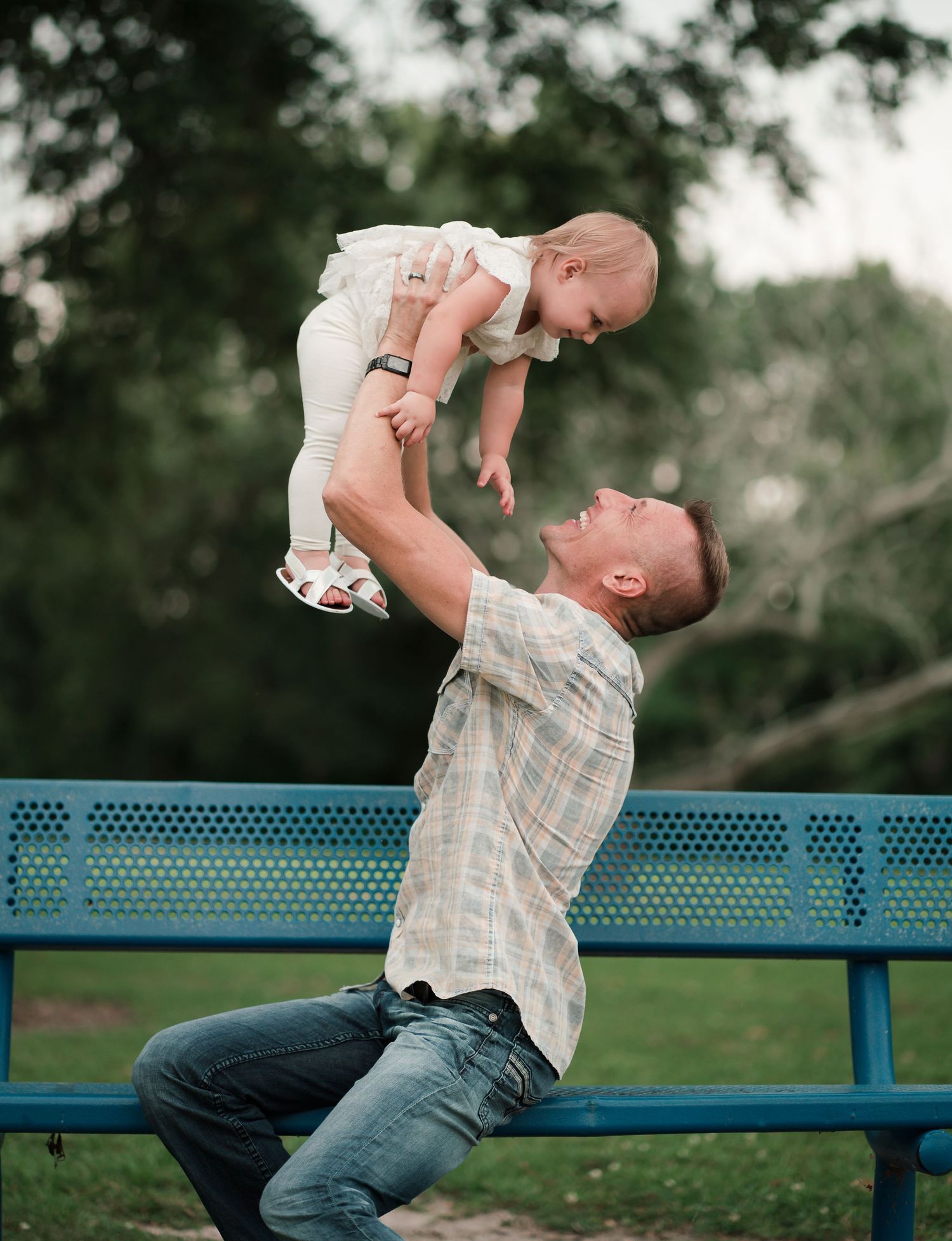 Playful moment on a park bench with a baby being lifted in the air.