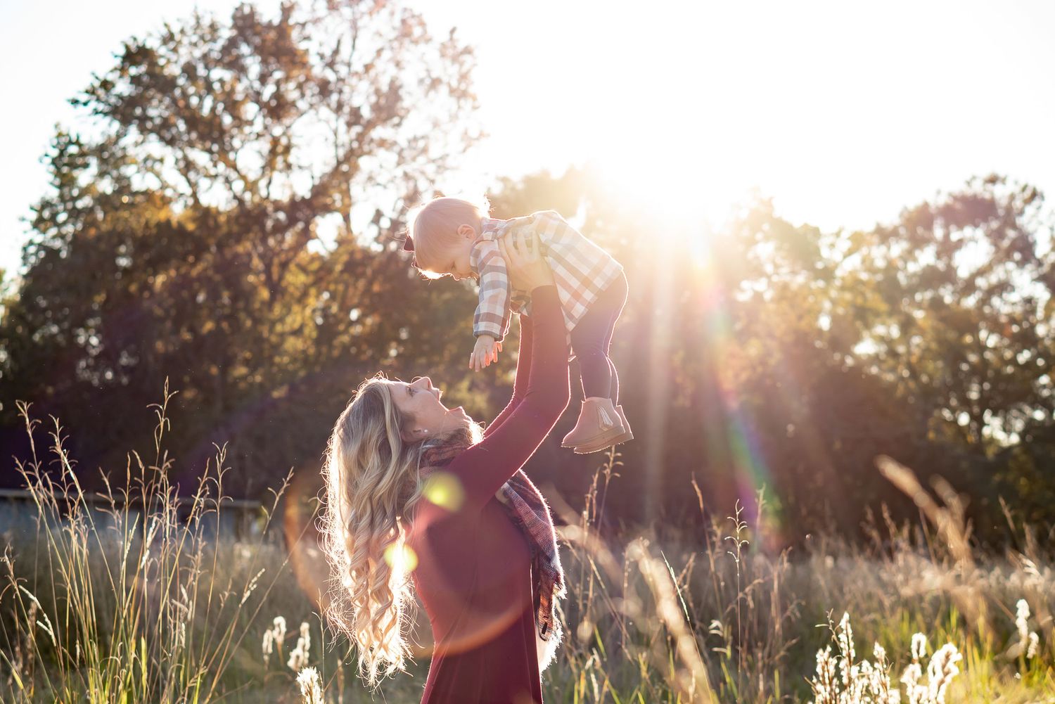 A silhouette of two figures playing in a sunlit field with tall grass at golden hour.