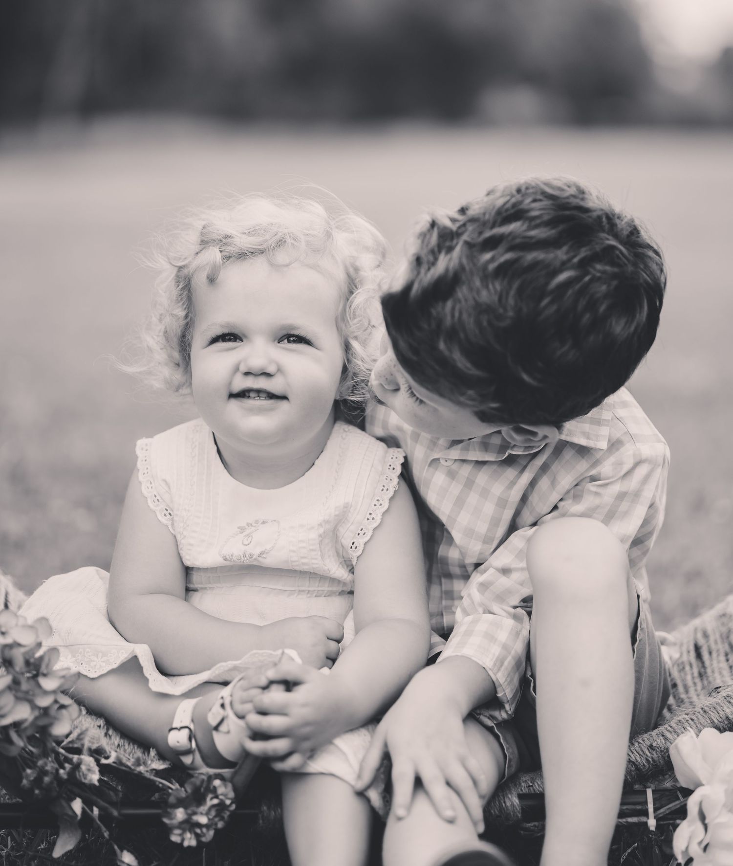 Sweet black and white photo of children sharing tender moment outdoors.
