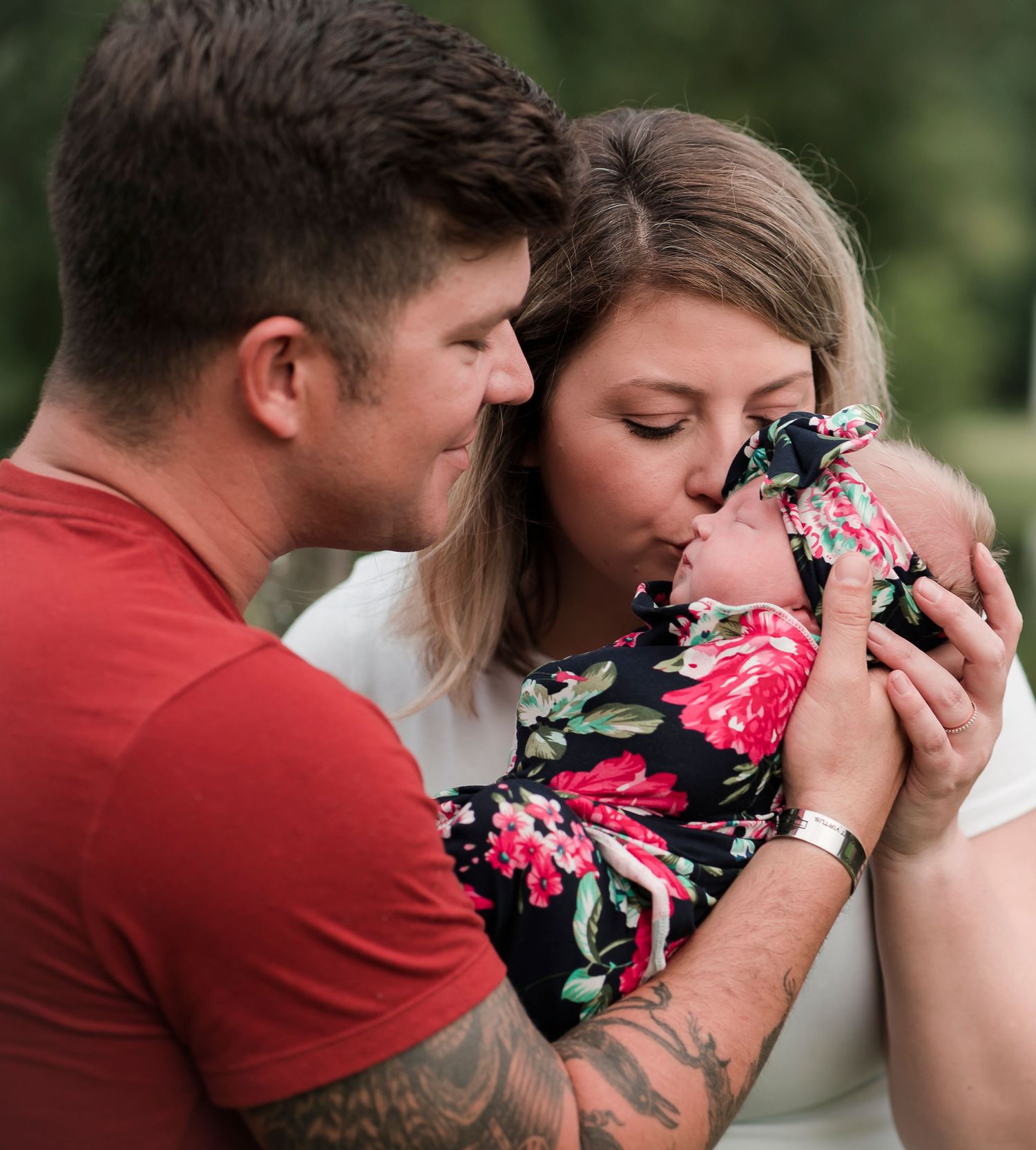 Tender moment as couple snuggles with baby in floral outfit outdoors.