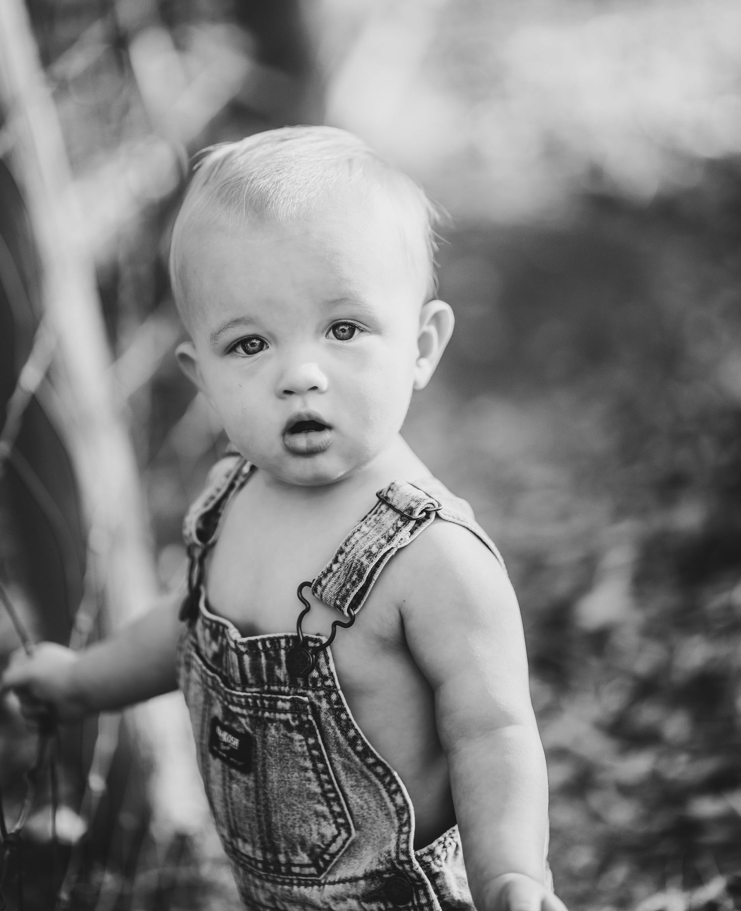 Portrait of toddler wearing denim overalls outdoors in black and white.