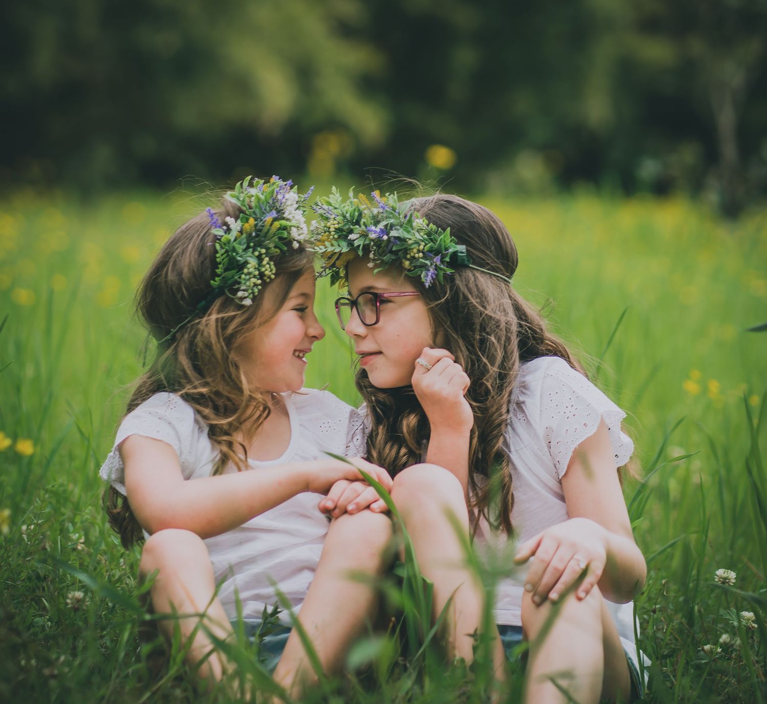 Two people wearing floral crowns share an intimate moment in a field of yellow flowers.