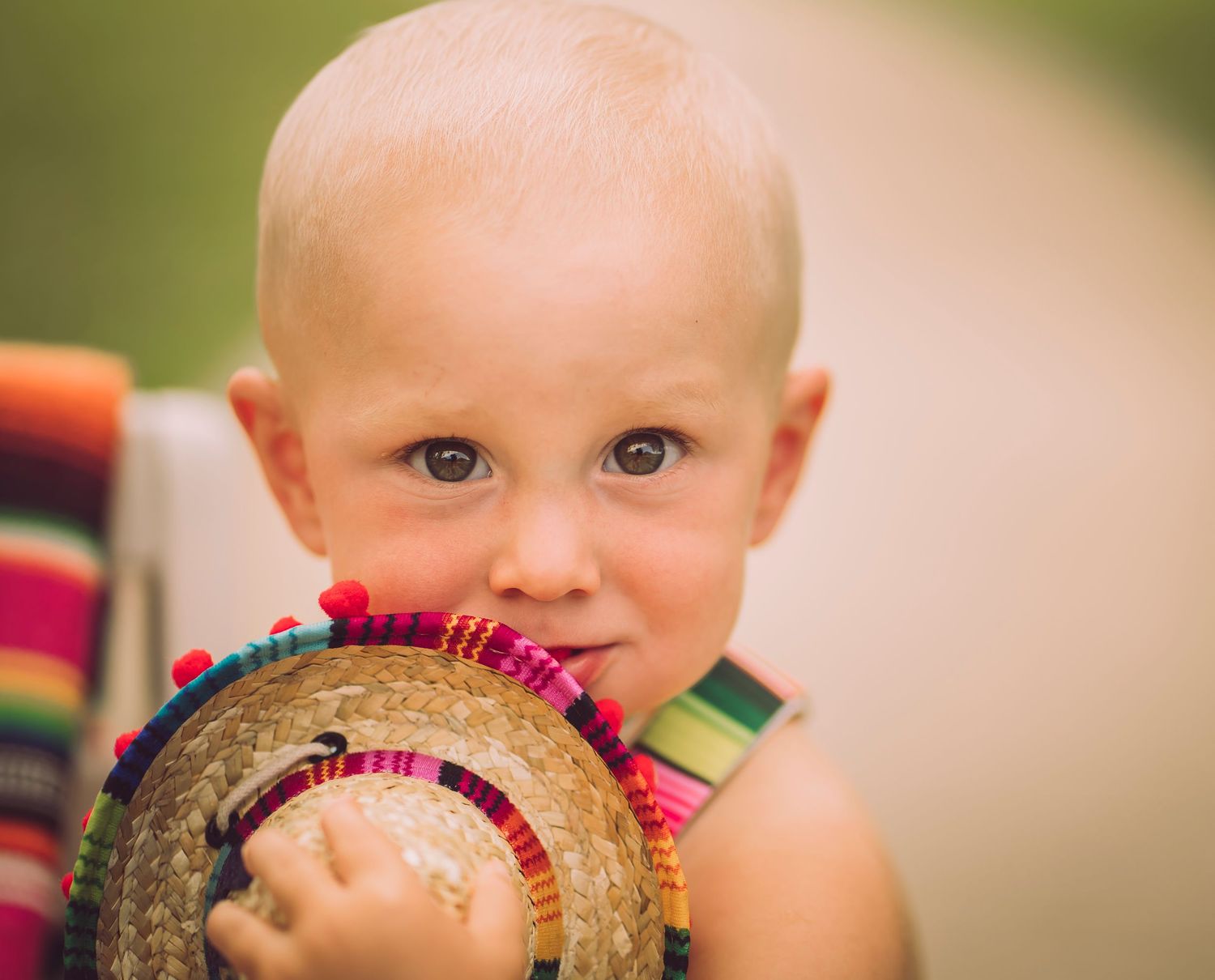 Baby in rainbow striped outfit holds decorative round object while looking at camera.