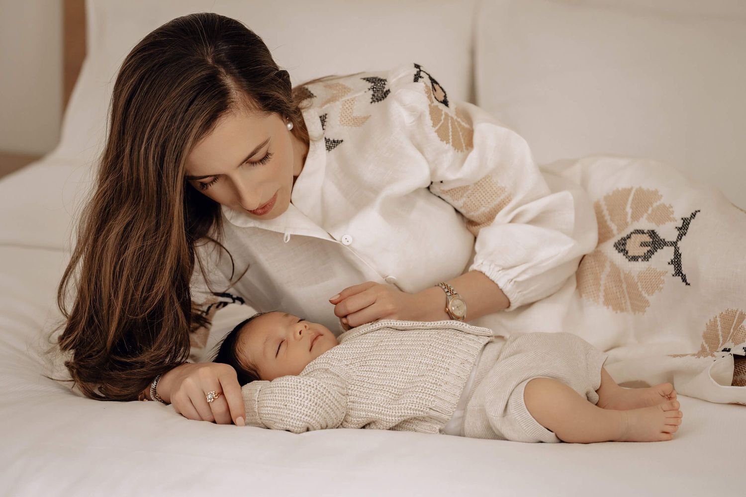 Intimate portrait of maternal bonding moment on white bedding in warm tones.