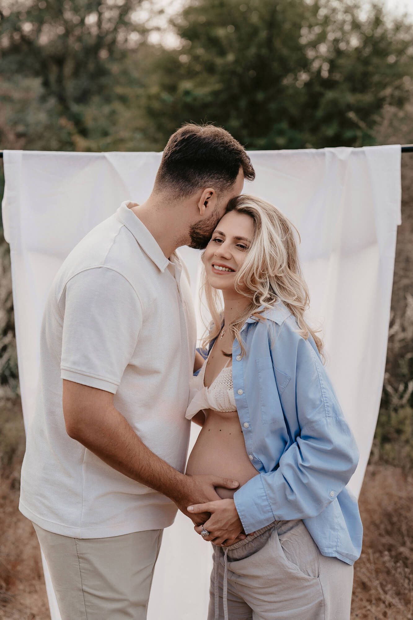Outdoor maternity photo with a couple sharing a tender moment against a white backdrop.