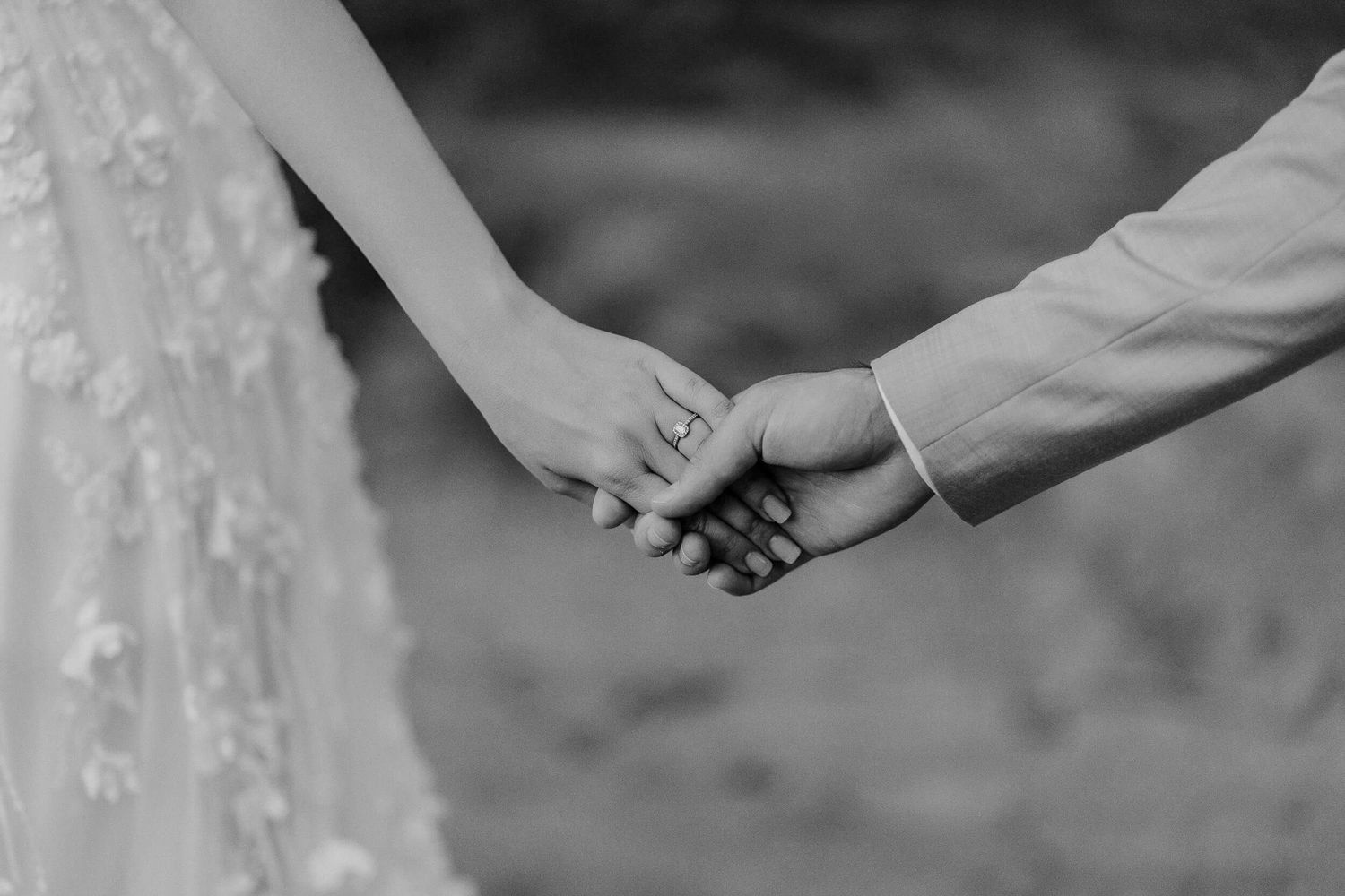 Black and white photo of couple holding hands with lace wedding dress visible showing tender wedding moment.