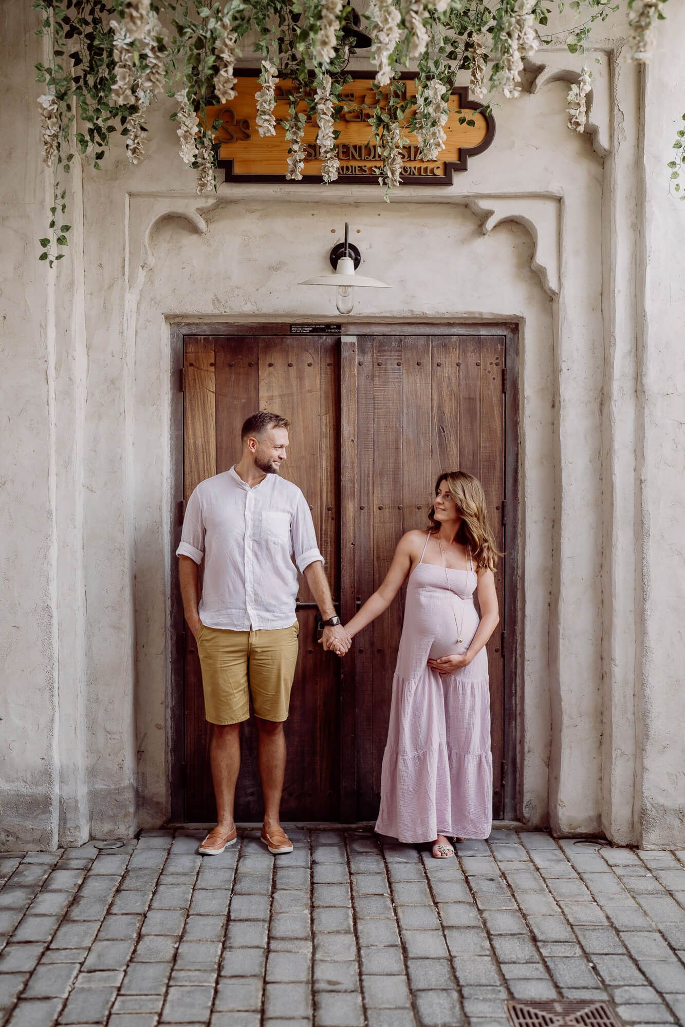 Couple standing in front of rustic wooden door with green vines hanging above in romantic outdoor setting.