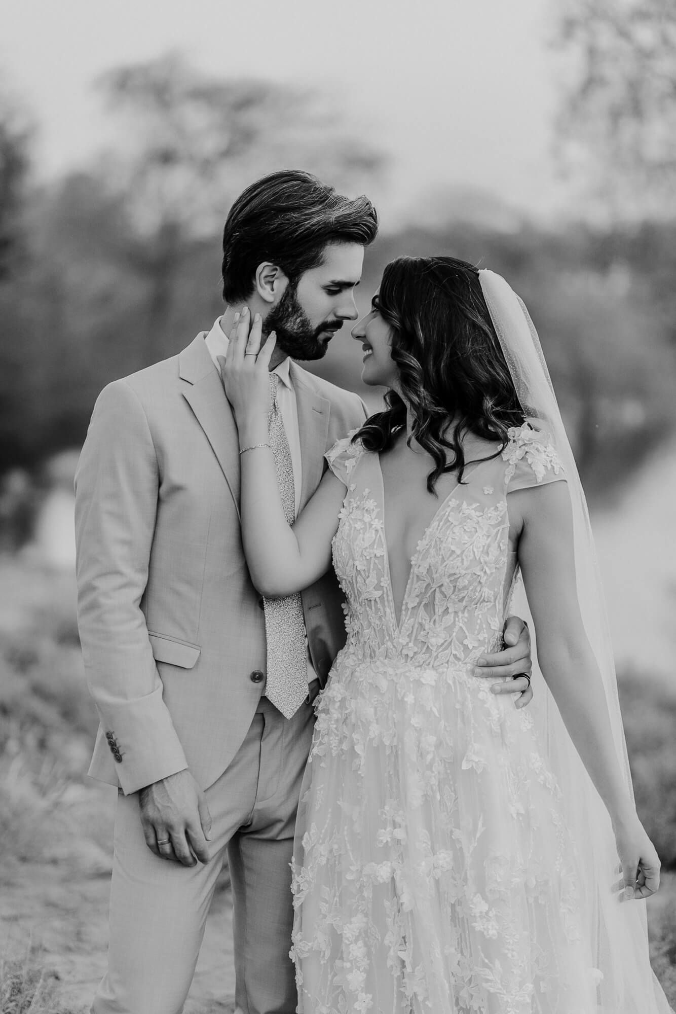 A romantic black and white wedding portrait of a couple embracing outdoors in formal attire.