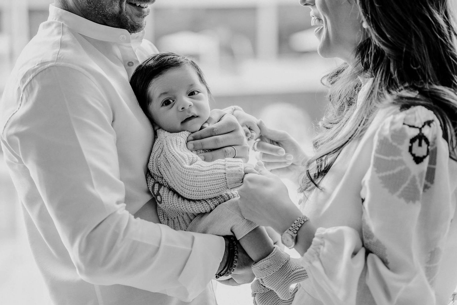 Black and white photo of parents holding their smiling baby in matching outfits.