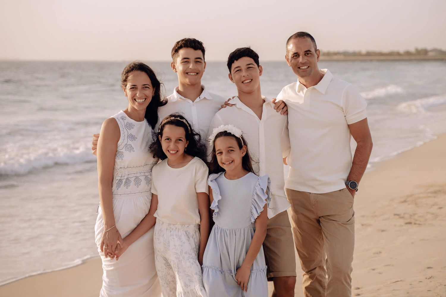 Casual family beach portrait with everyone wearing coordinated white and neutral colors.