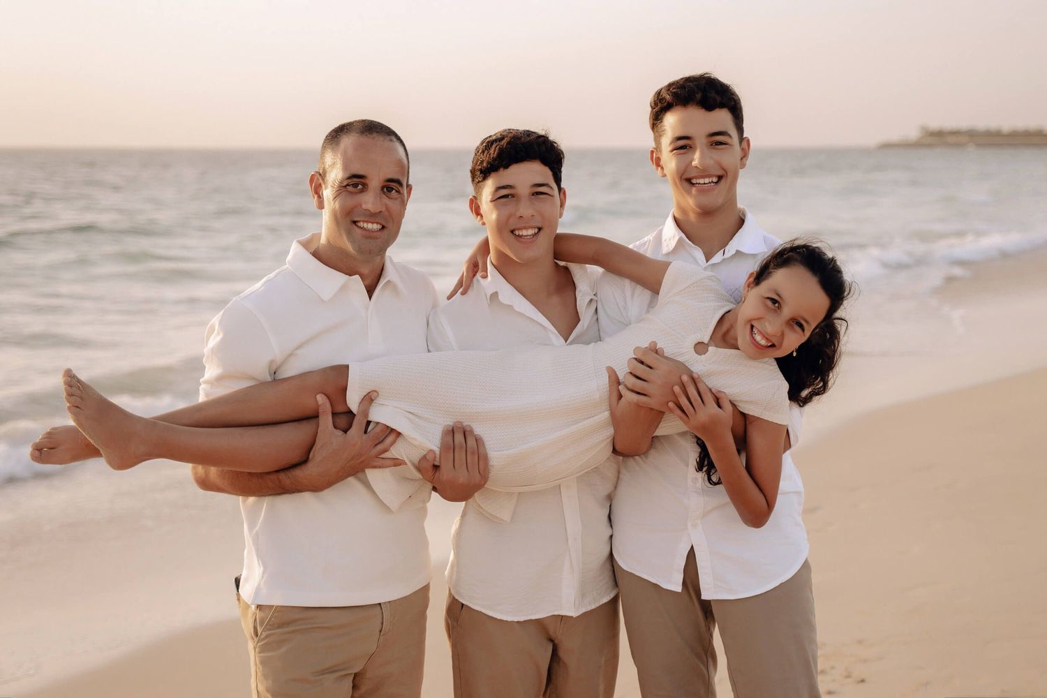 Family group poses together on beach wearing white shirts and khaki shorts at sunset.