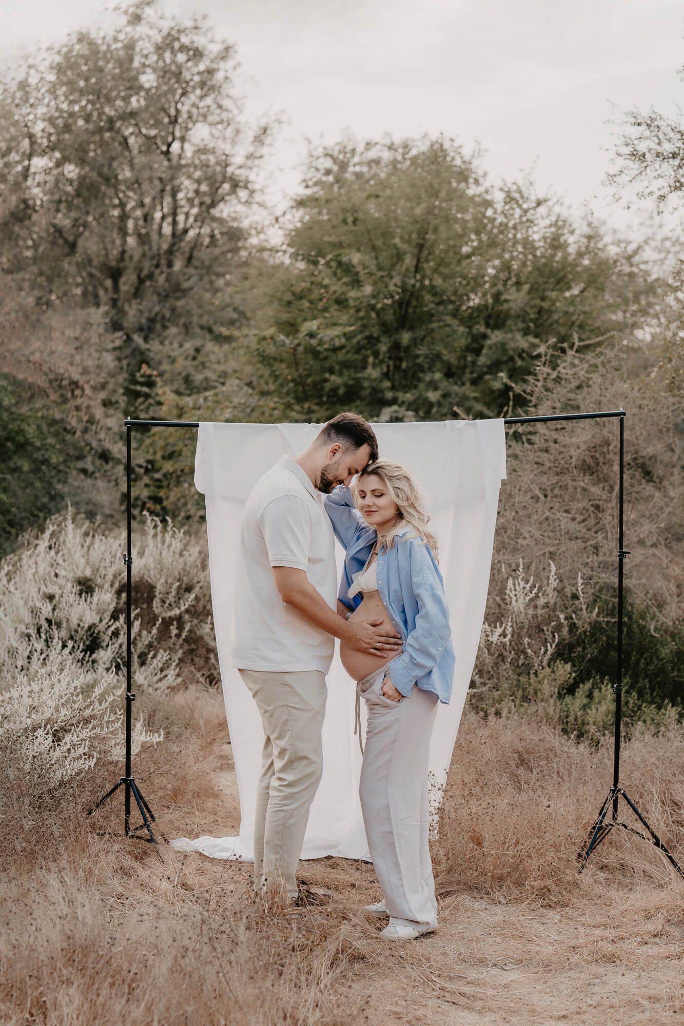 Couple embracing in front of a white photography backdrop outdoors in a desert landscape.