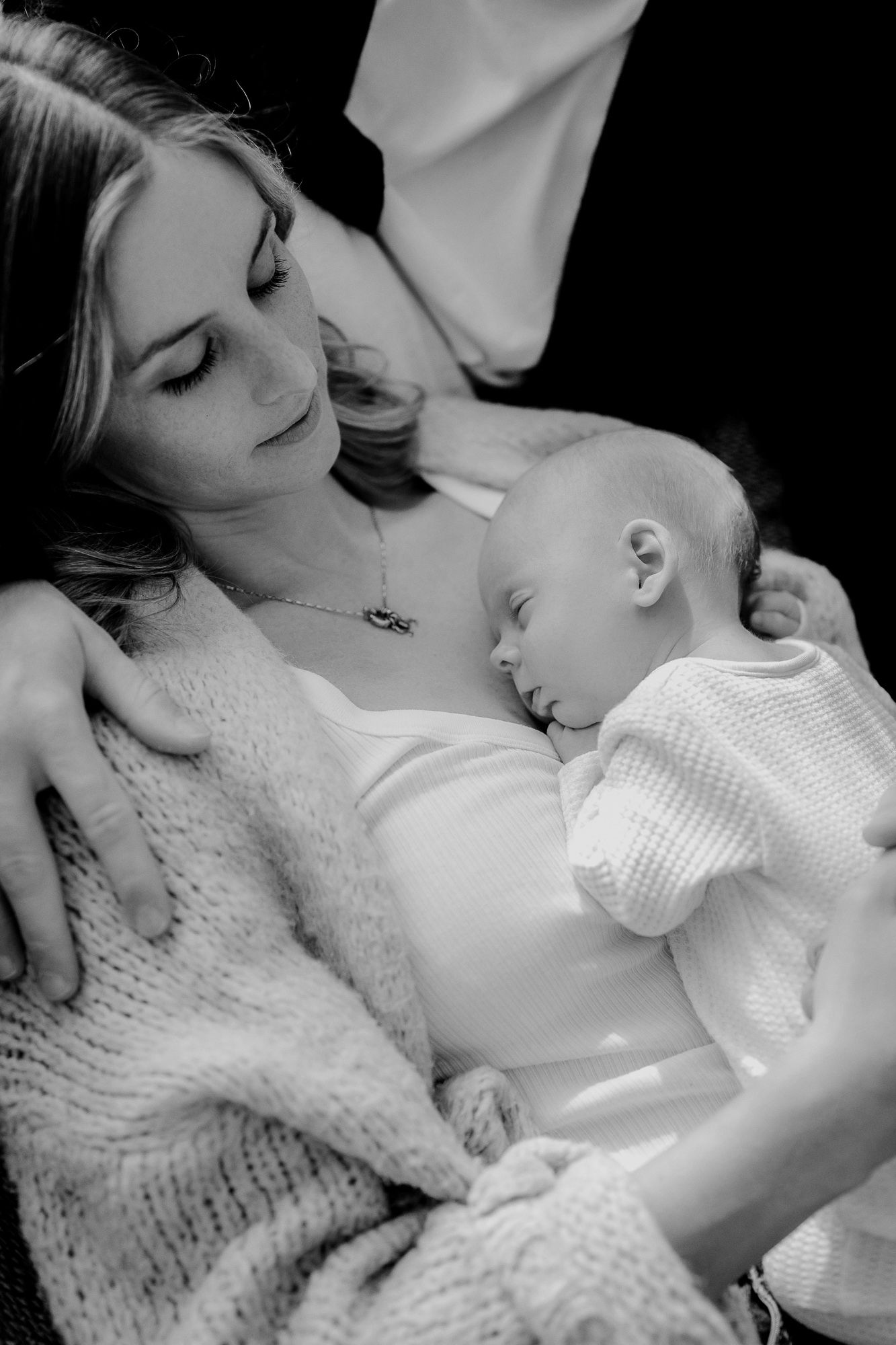 A tender black and white moment captured as a sleeping baby rests peacefully against someone in a cozy knit sweater.