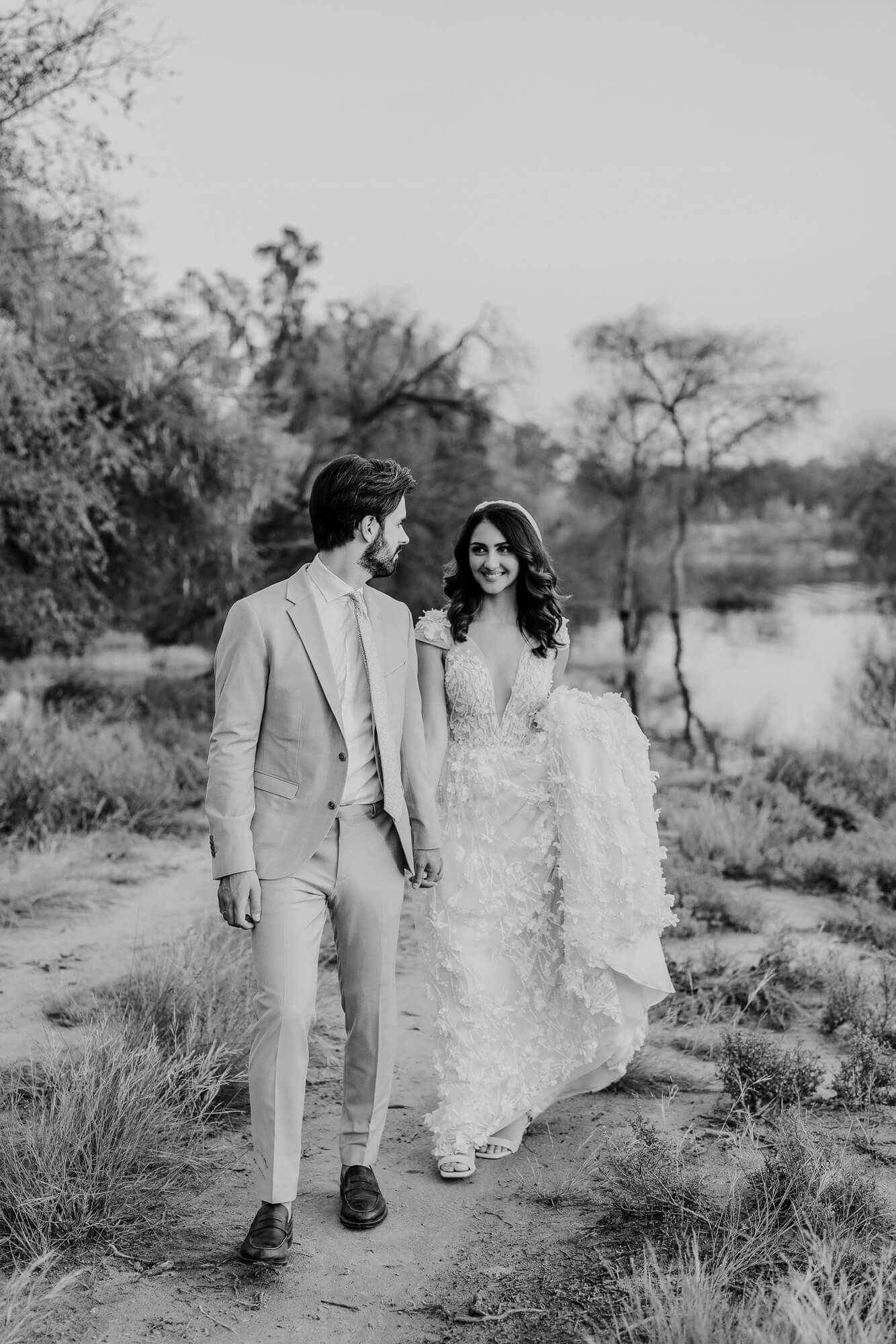 Black and white photo series of a couple in wedding attire walking together on a desert path through natural brush.