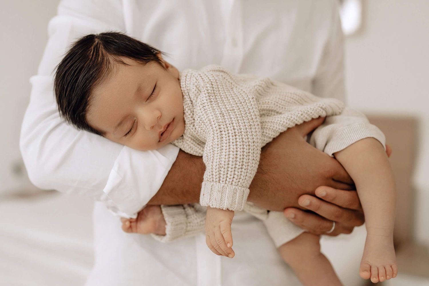 Tender moment of sleeping baby being held in cream knit sweater.