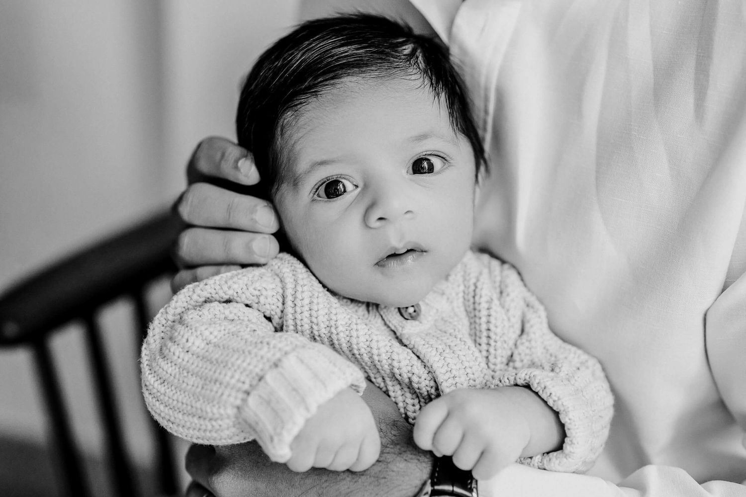 Black and white portrait of baby in knit sweater looking towards camera.