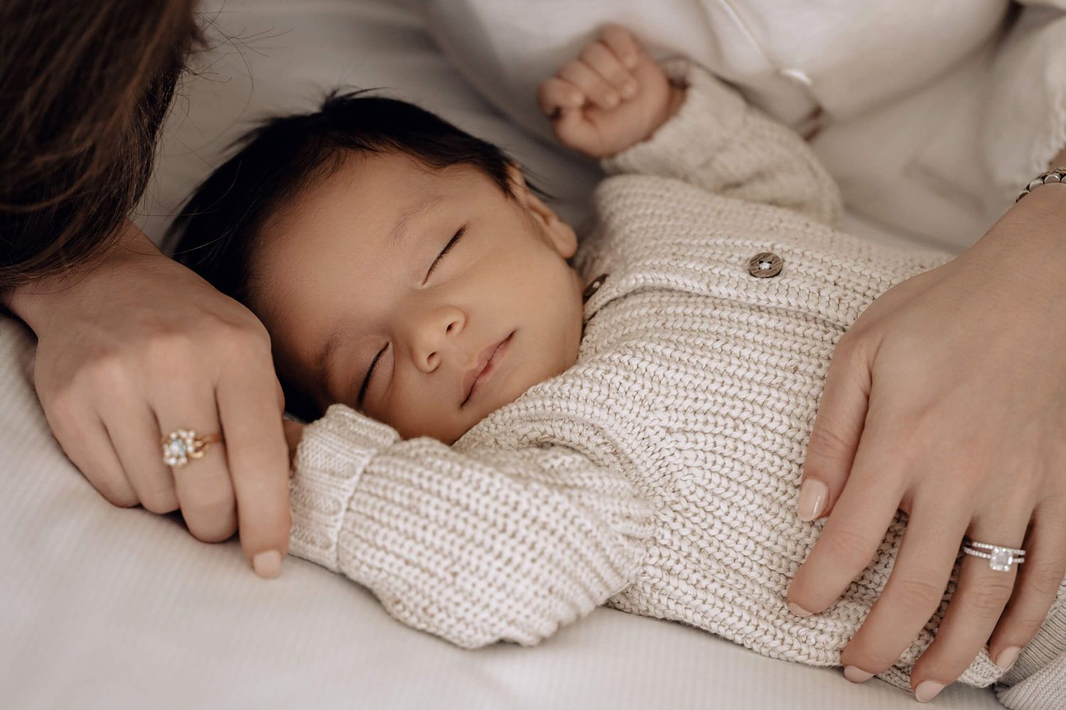 Close-up of sleeping infant in knit sweater with hands gently resting nearby.