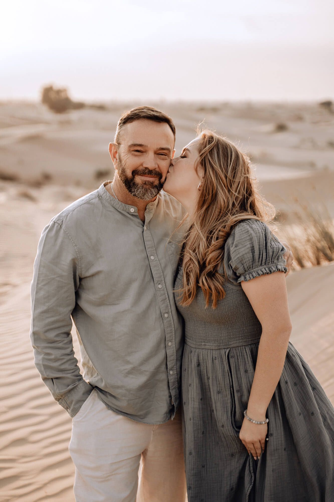 Loving couple shares tender moment against backdrop of rolling desert sand dunes.
