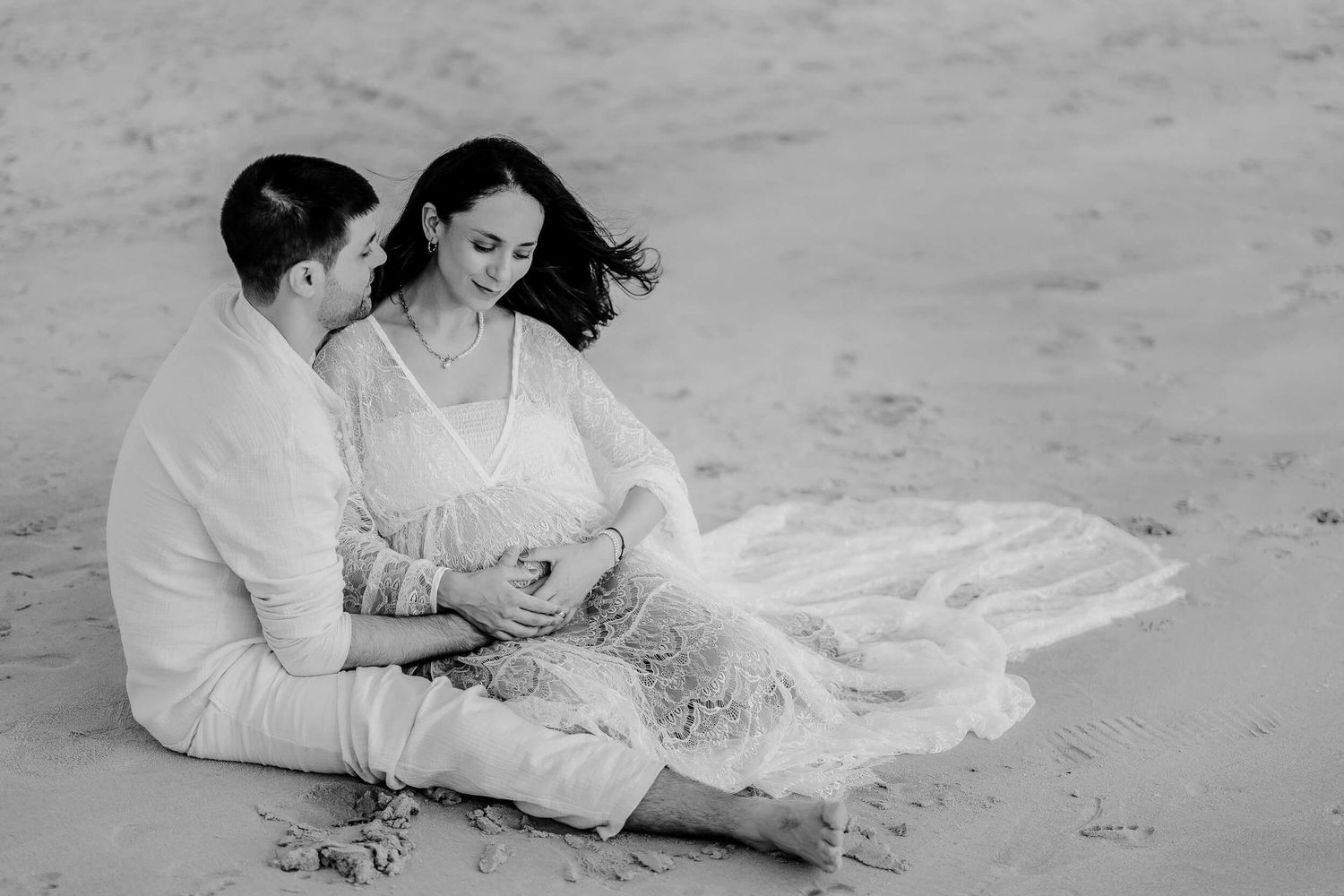 A couple sits together on the beach sharing a romantic moment in black and white photography.