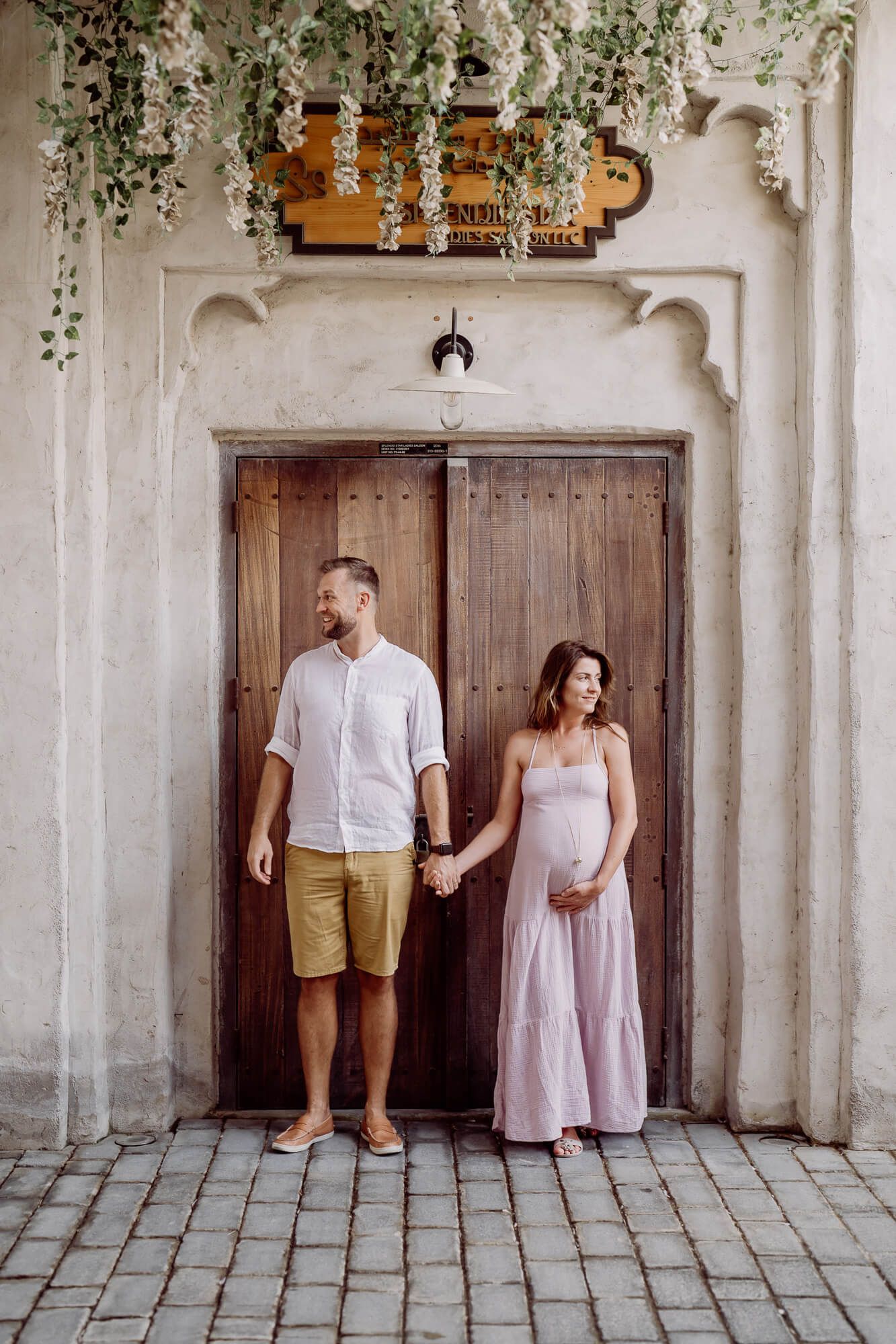 A couple poses against a white stone wall with decorative archways and hanging greenery in a series of four photos.