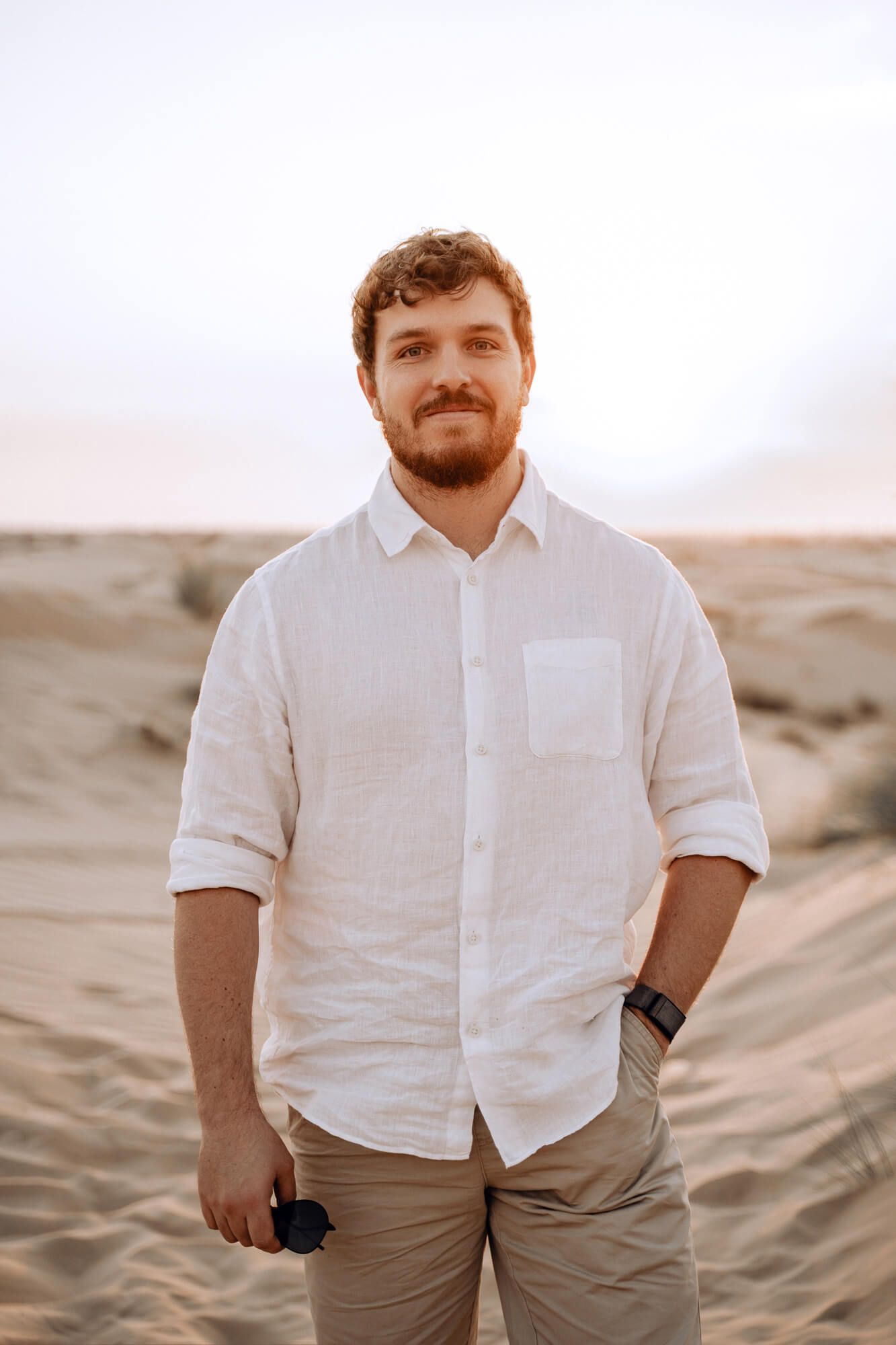 Portrait of person in white button-down shirt standing against desert landscape backdrop.