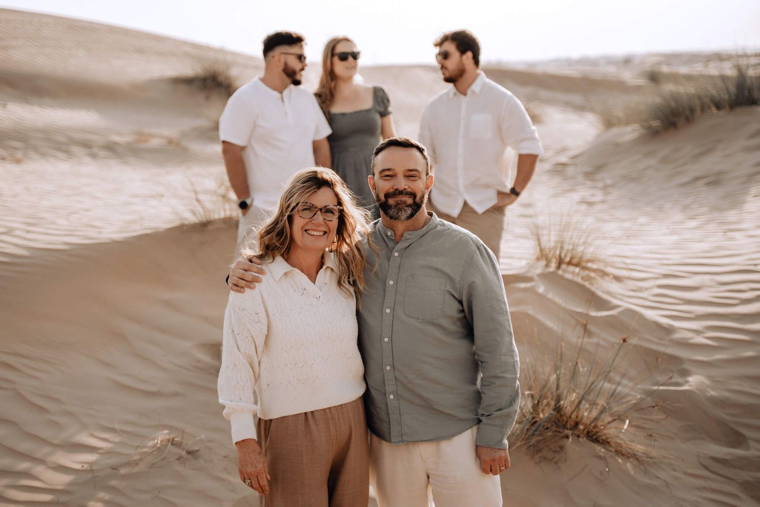 Group of friends in neutral colored clothing posing together on desert sand dunes.