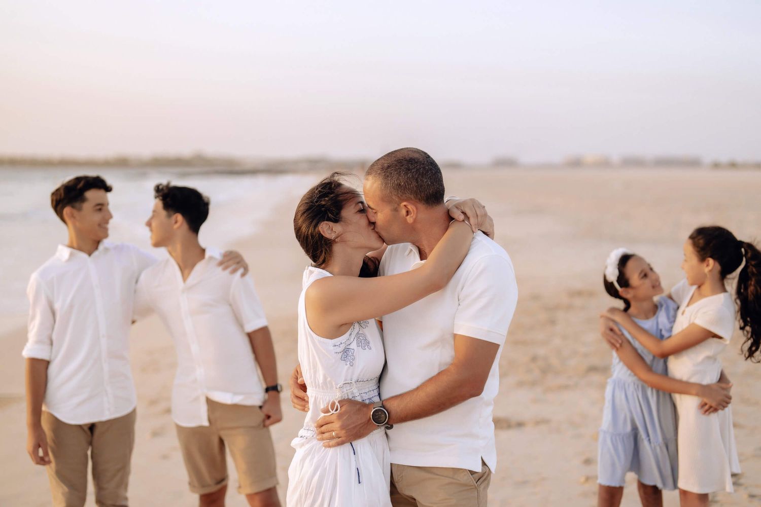 Three couples showing affection on sandy beach during sunset photo session.