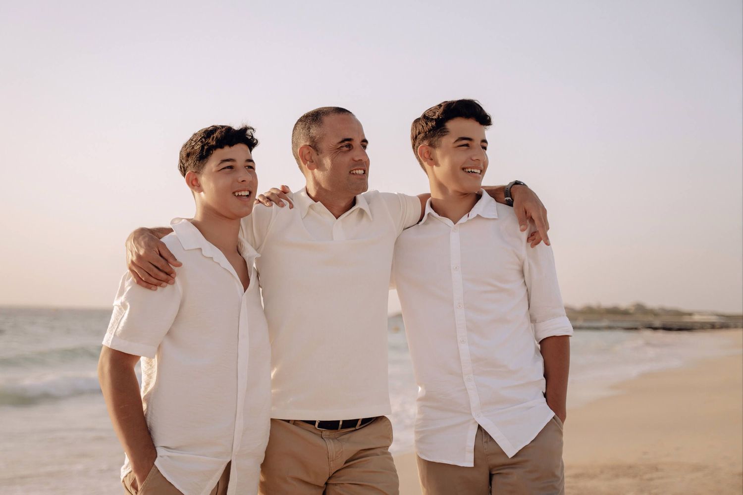 Candid beach portrait of people in coordinated white outfits standing together near the ocean.