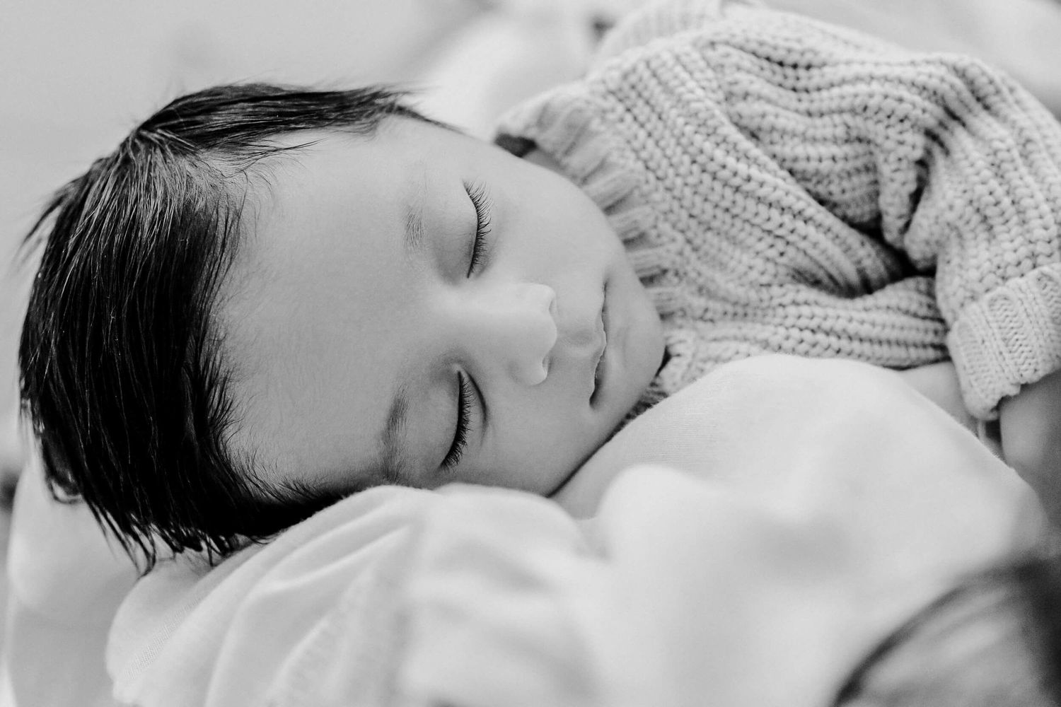 Peaceful portrait of sleeping infant in cream knit sweater.