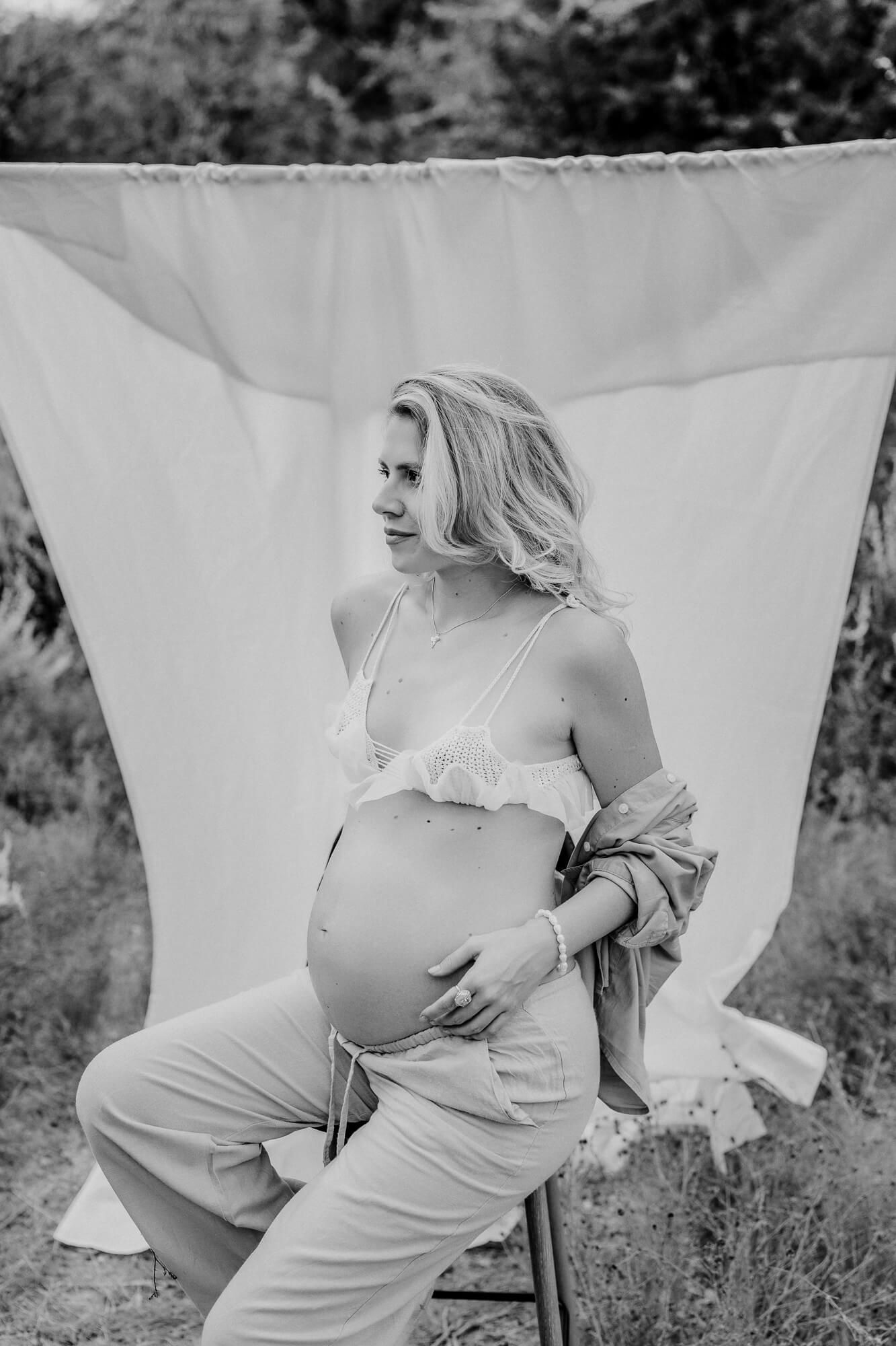 Black and white maternity portrait with white backdrop and casual styling.