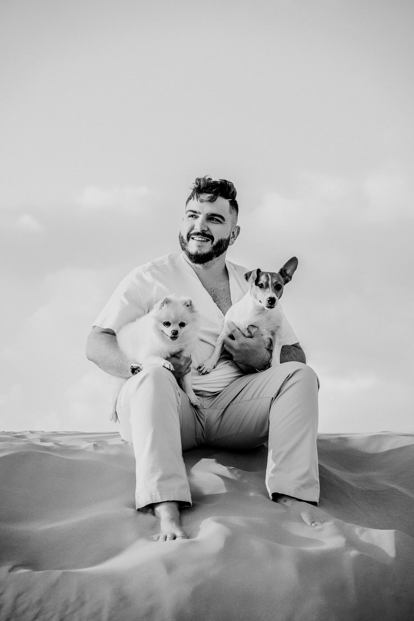 Black and white photo of small dogs on desert sand dunes with cloudy sky.