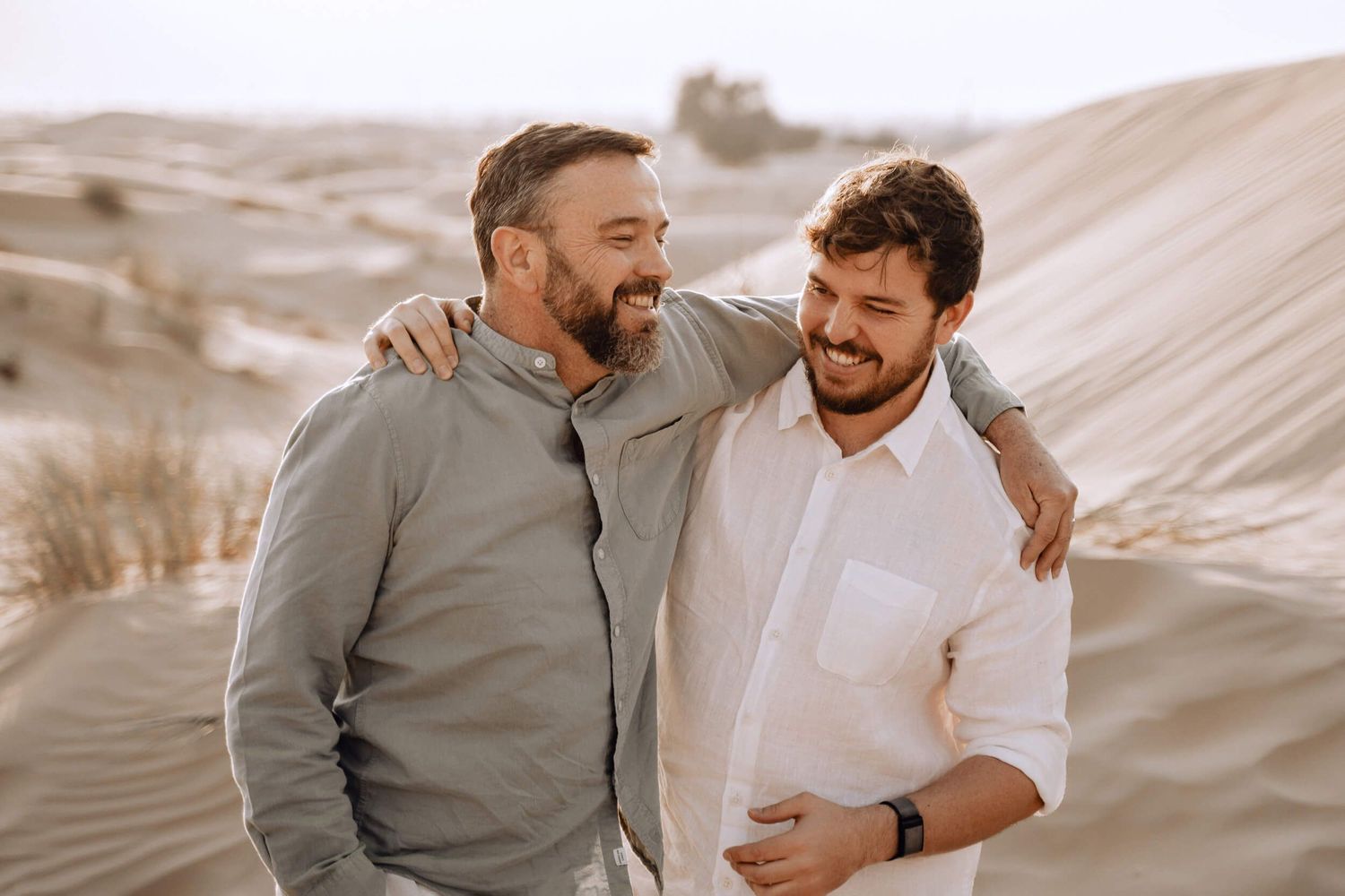 Desert engagement photo with two people embracing and smiling in neutral tones.
