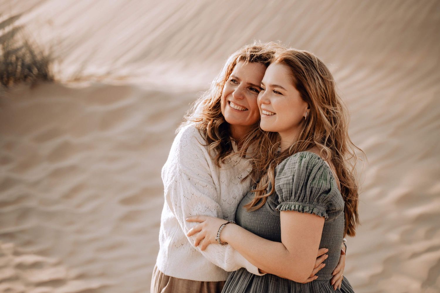 Two people share loving embrace while standing in front of desert sand dunes.