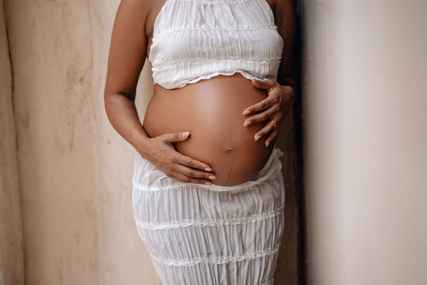 Maternity photos in white clothing showing close-up details of a pregnant belly.