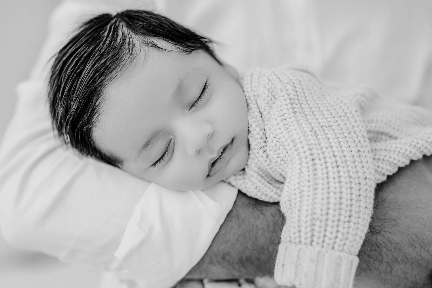Tender monochrome portrait of family members resting together on white sheets.