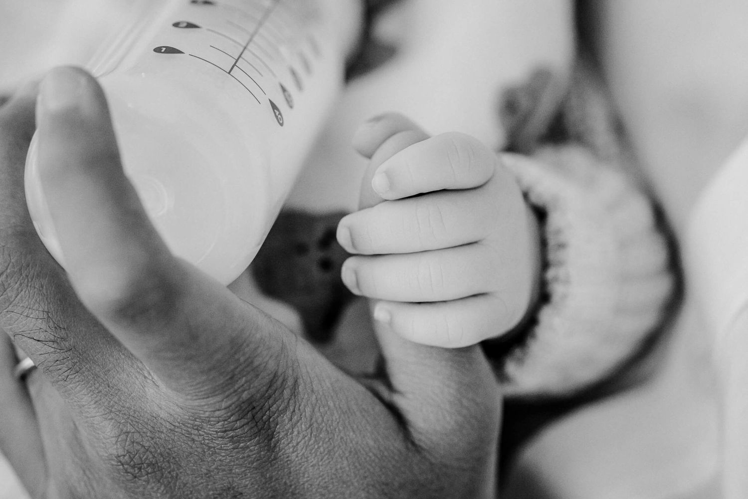 A newborn baby's tiny hand grasps a finger in black and white.