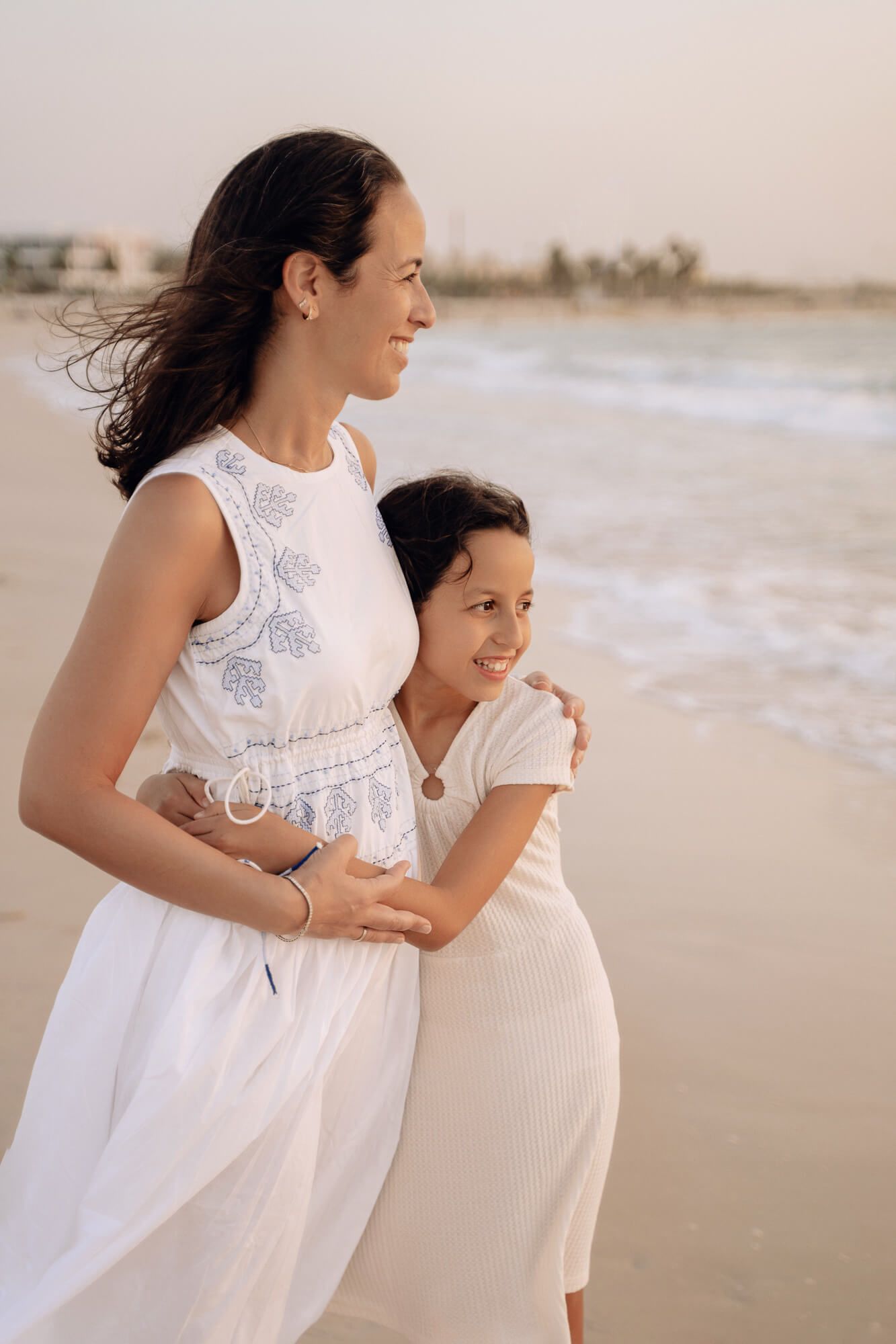 A white lace dress and cream outfit stand out against the serene beach backdrop at sunset.