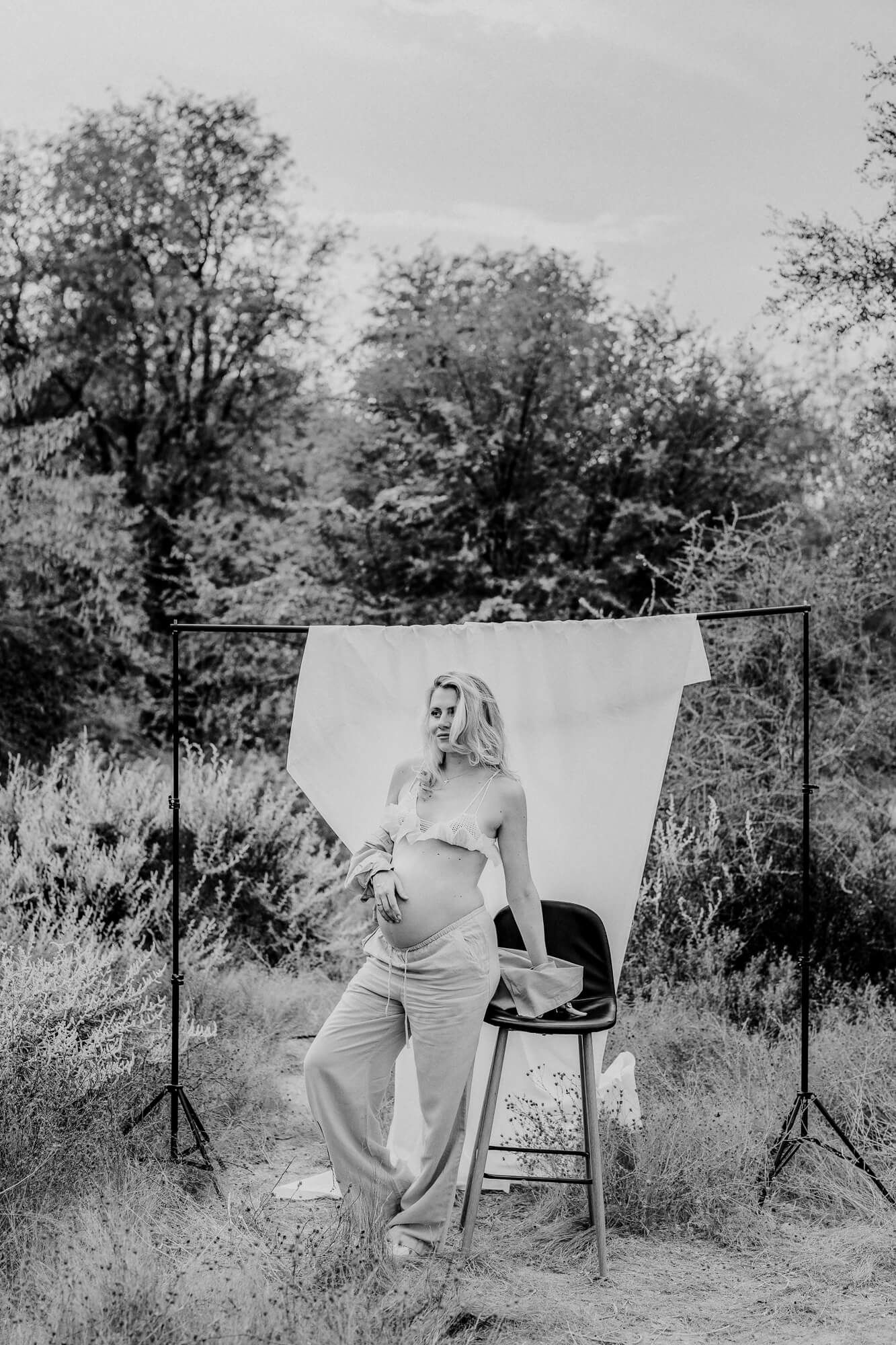Outdoor photography setup with white backdrop and chair against natural foliage.