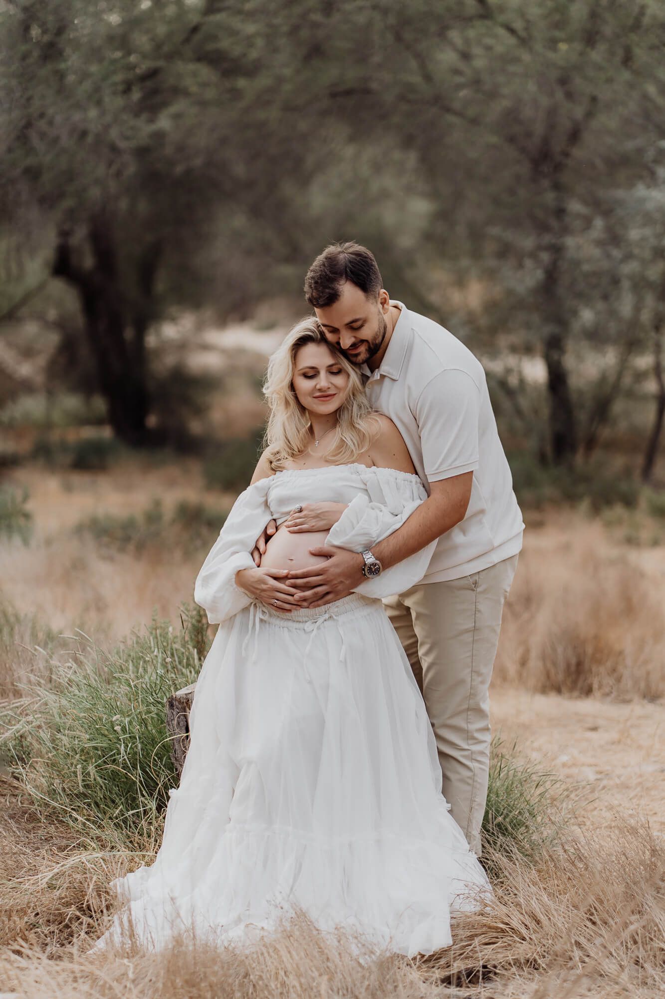 A tender maternity moment captured between expectant parents in a rustic outdoor setting.