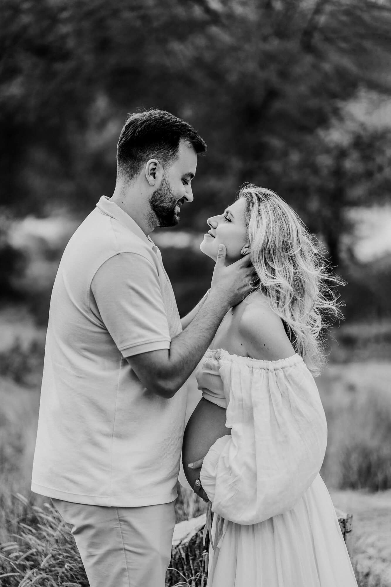 Black and white maternity series capturing playful moments between couple outdoors.