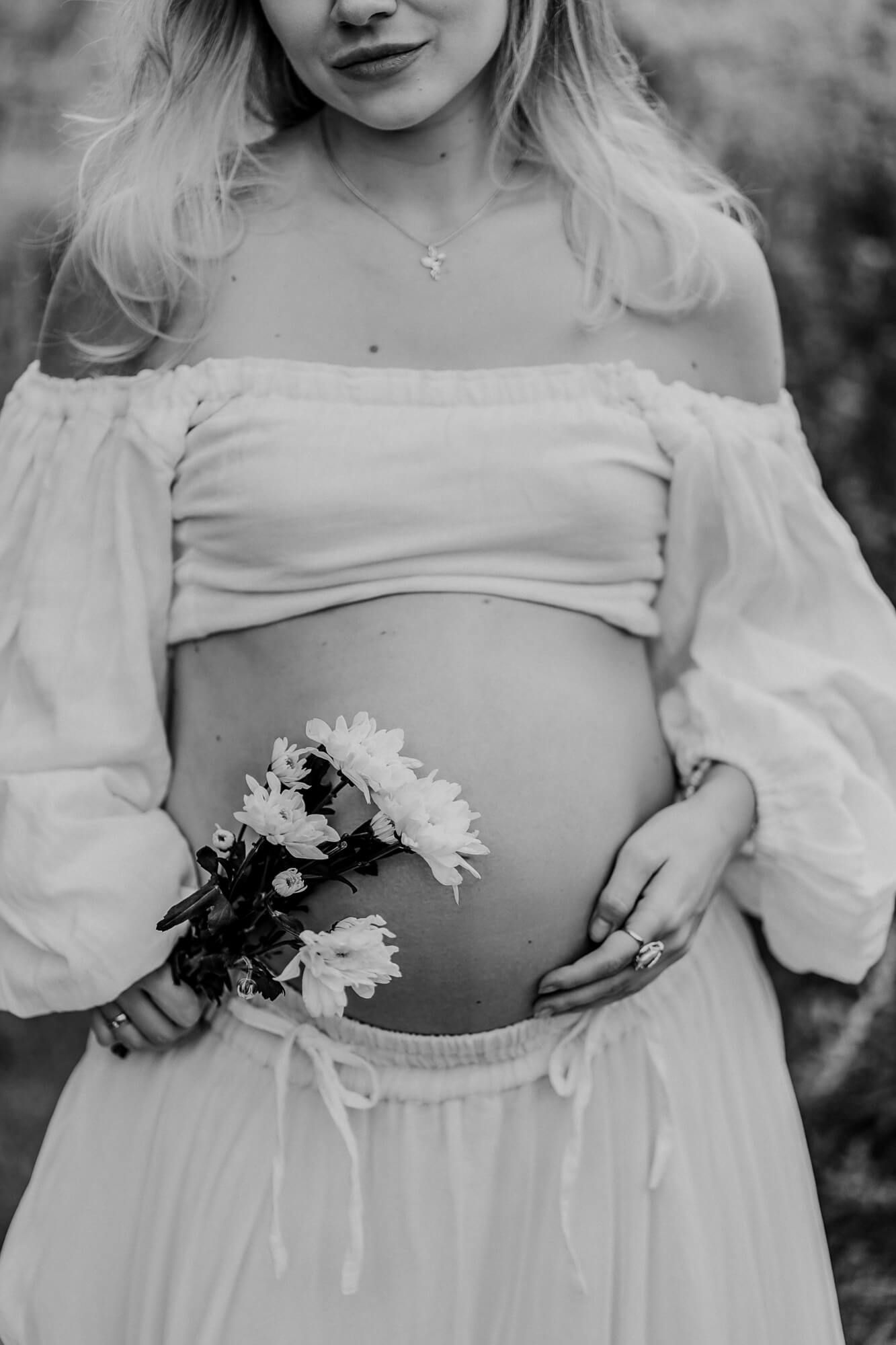 Close-up maternity photo showing details of white dress and delicate flowers against bare belly.