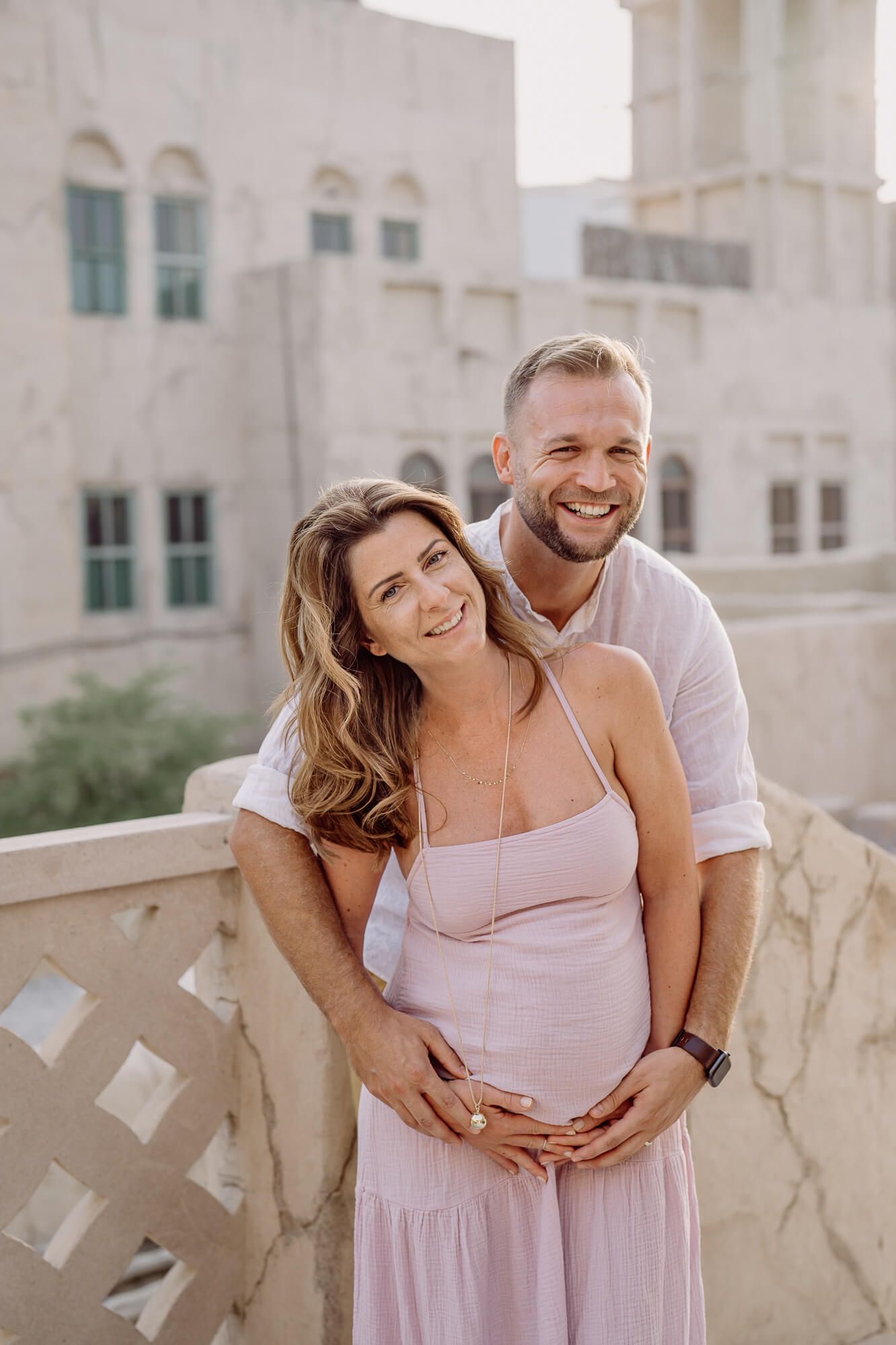 An expecting couple shares loving moments in a series of romantic outdoor maternity photos against a white building.