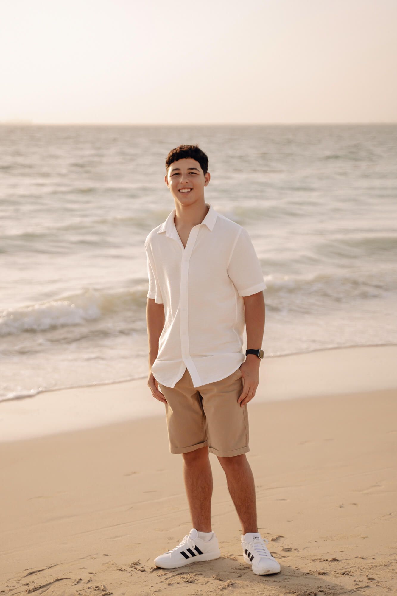 Person wearing white shirt and khaki shorts standing on beach with ocean waves in background.