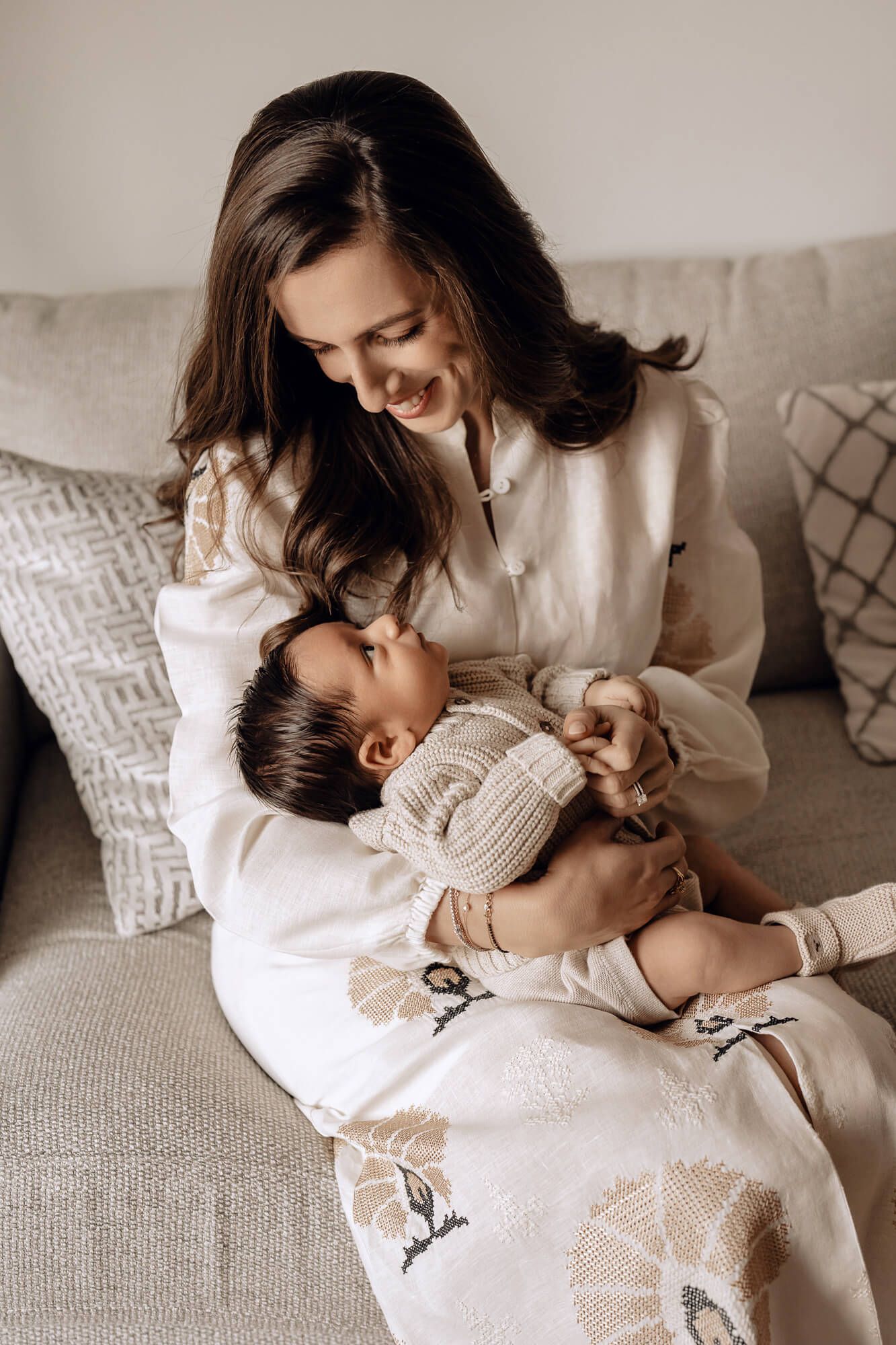 Series of loving interactions between parents and baby on a grey couch in soft lighting.