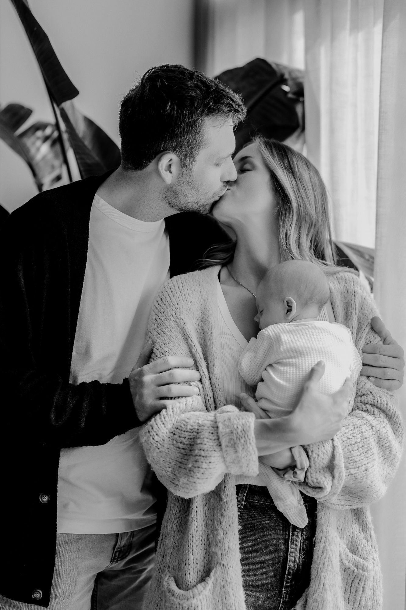 A tender black and white intimate moment between a couple holding their baby in a cozy indoor setting.